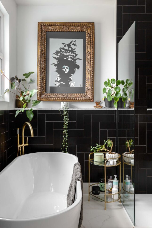 Freestanding bathtub against black tiled wall with brass fixtures and framed artwork — interior photography for Architecture:WK, London