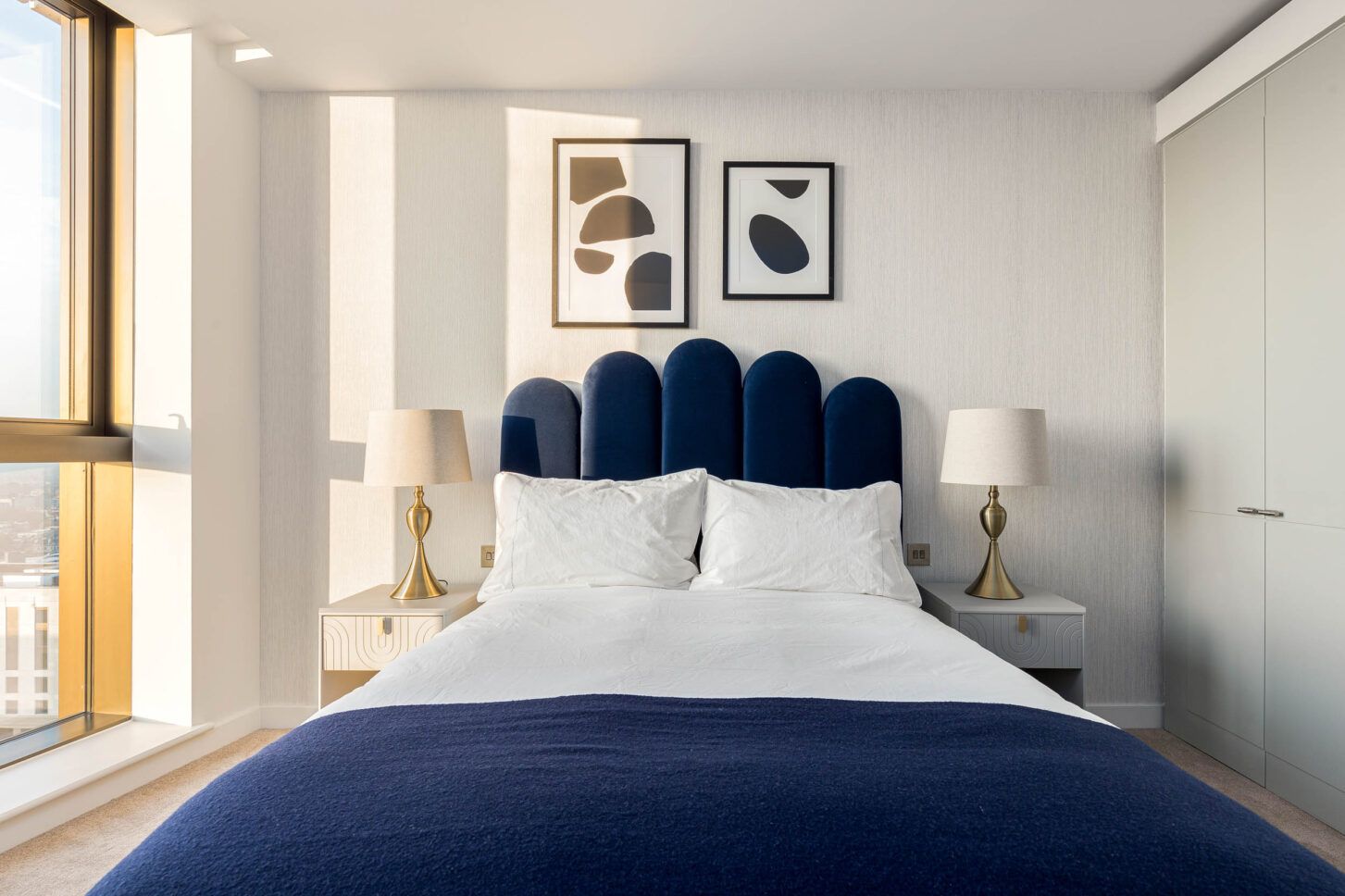 Bedroom with navy velvet scalloped headboard and floor-to-ceiling city-view windows — interior photography for Housedesigner, London