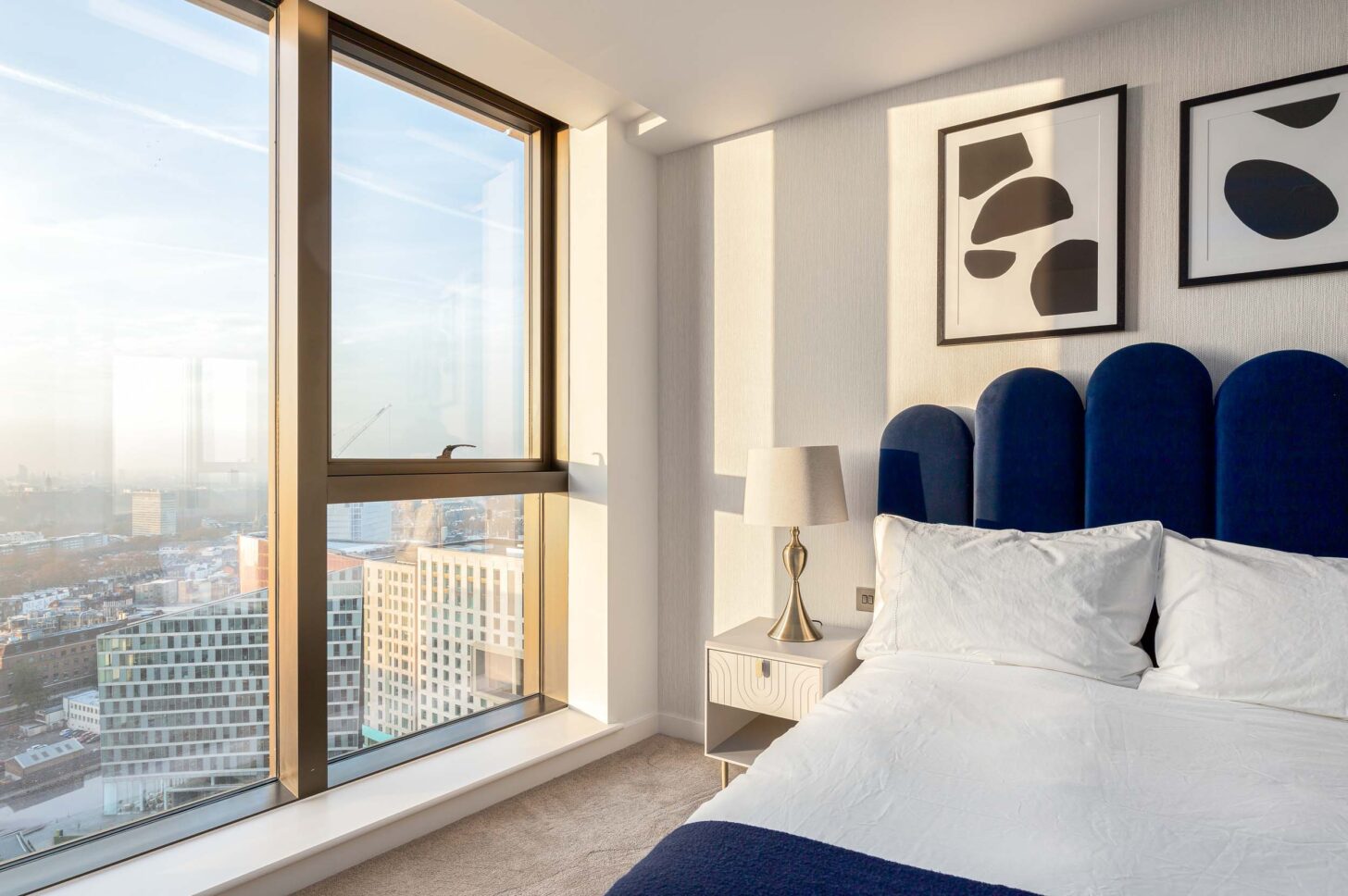Bedroom with navy velvet scalloped headboard overlooking London skyline through floor-to-ceiling windows — interior photography for Housedesigner, London