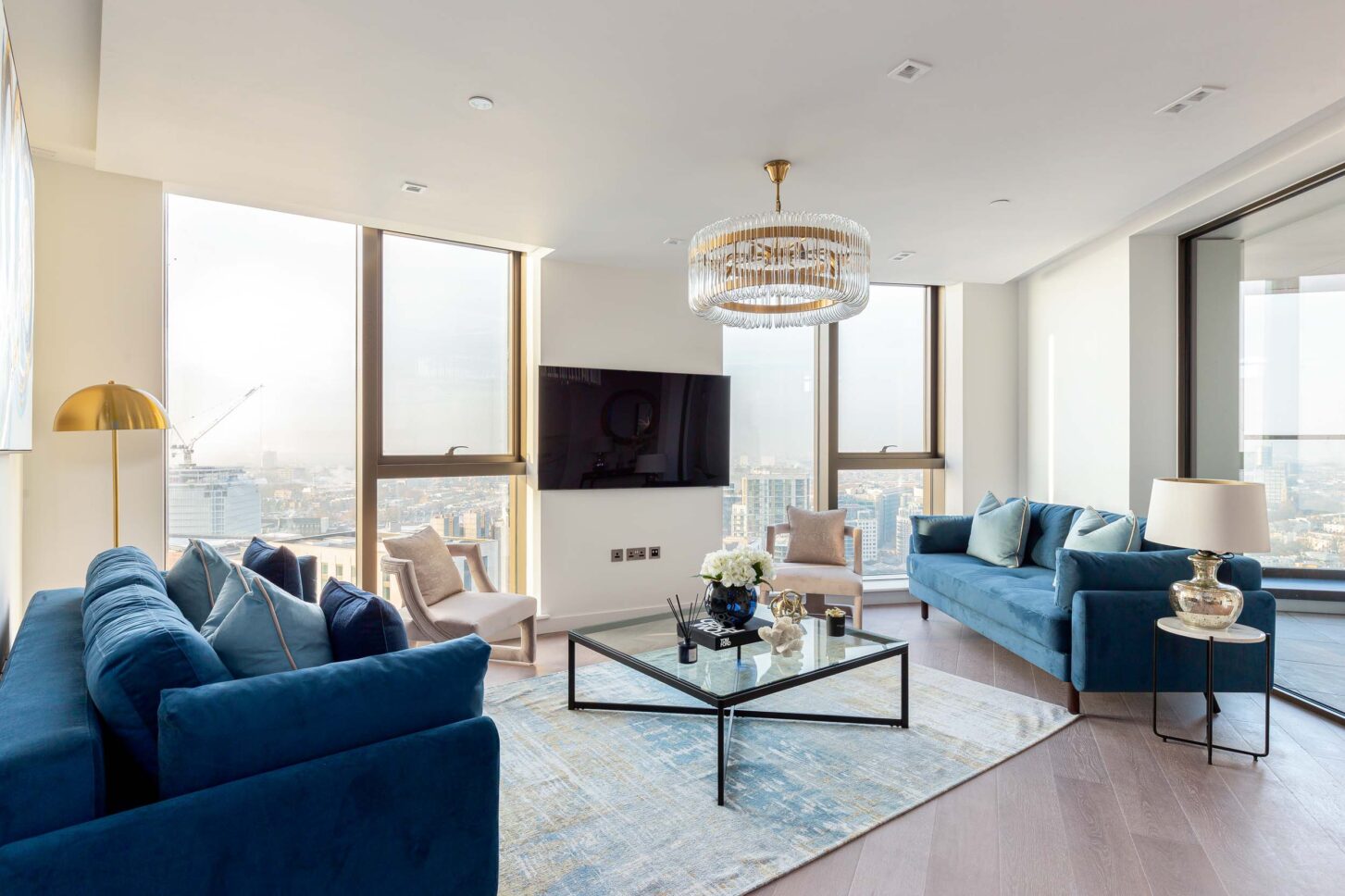 Living room with blue velvet sofas and gold pendant chandelier overlooking London skyline — interior photography for Housedesigner, London