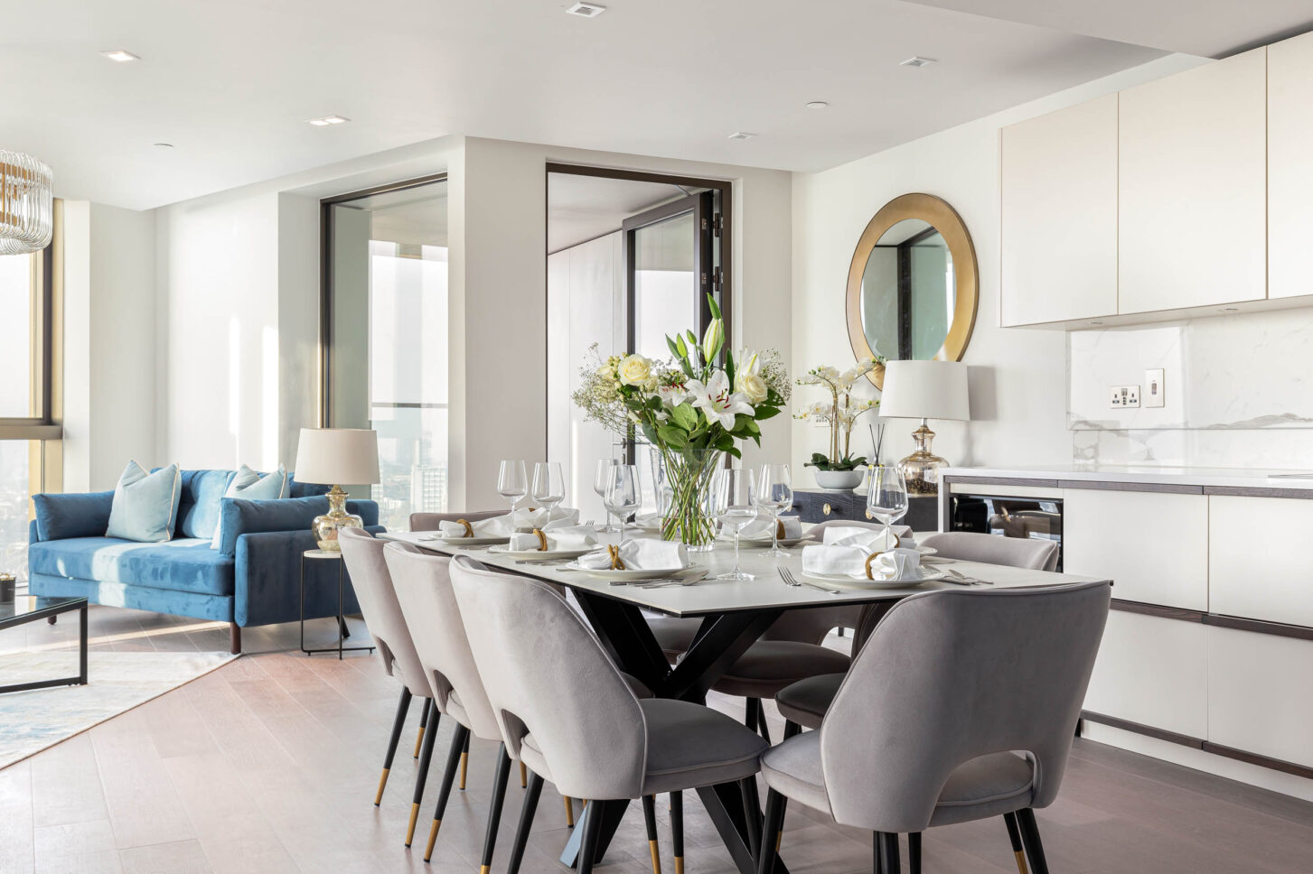 Open-plan dining and kitchen with round mirror, styled table and blue sofa beyond — interior photography for Housedesigner, London
