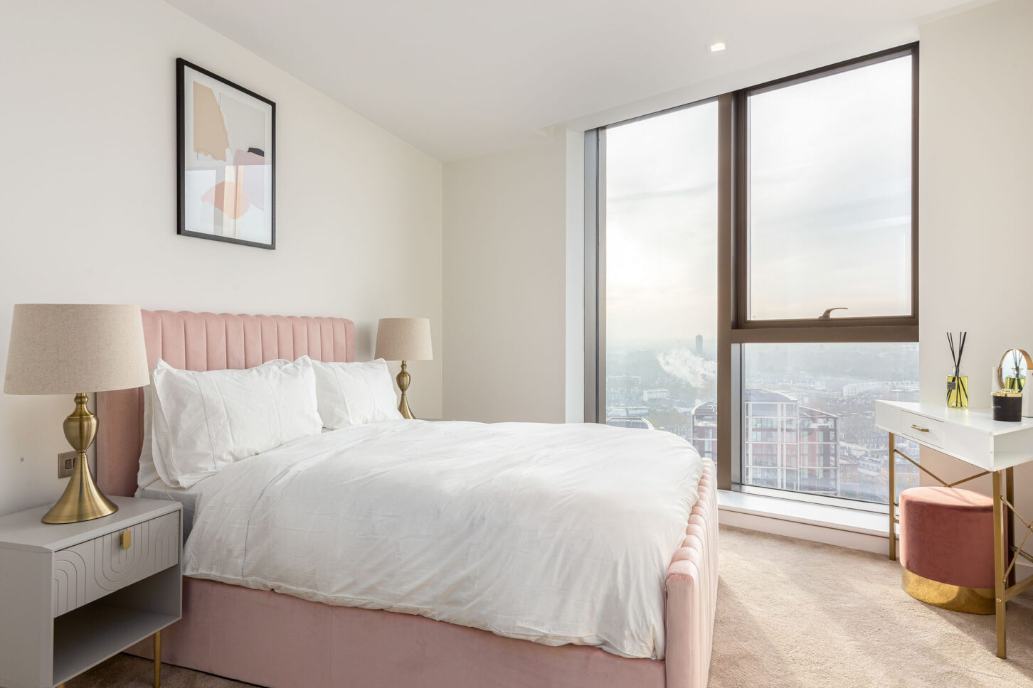 Bedroom with blush pink upholstered bed, gold-legged desk and floor-to-ceiling city views — interior photography for Housedesigner, London