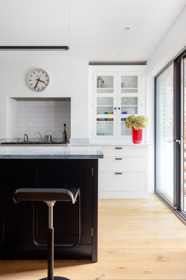 Kitchen with dark island and marble worktop opening onto garden — Hoban Design, Wimbledon Village