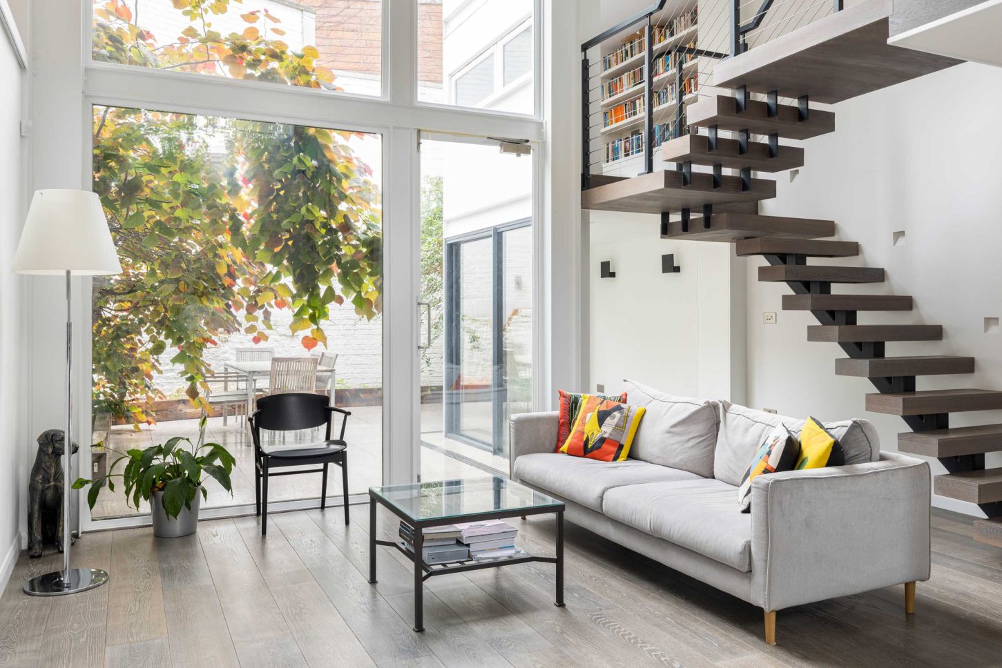 Double-height living room with floating staircase and built-in bookshelf, opening to garden — Canonbury, designed by Unknown Makers, London